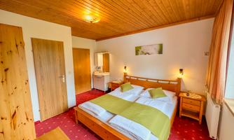A cozy bedroom with a double bed and wood paneling. The room is bright and cheerful with a small table and a wash area.