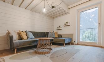 A cozy living space with a blue sofa and a round coffee table. Large windows offer a view of the mountains.