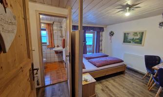 A cozy bedroom with a double bed and wooden decor. A bathroom is visible in the background.