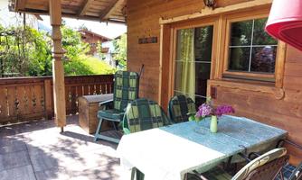 A cozy balcony with a table and chairs. Fresh flowers are on the table and the sun is shining on the wooden paneling.