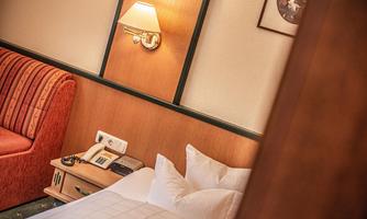 A cozy hotel room with a bed and a red sofa. The walls are painted in warm colors and there is a bedside lamp.