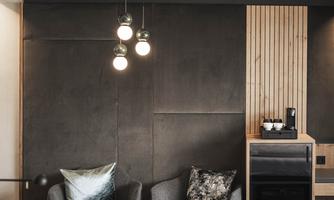 A modern room with two cozy armchairs and a small table. The wall is made of wood and has appealing lighting.