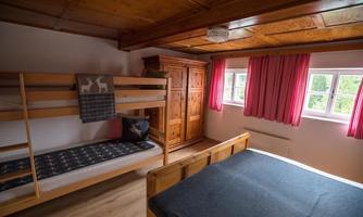 A cozy bedroom with a bunk bed and a double bed. The walls are in warm colors and the windows are outfitted with red curtains.