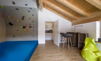A modern room with a climbing wall and a blue climbing area. In the corner, there is a cozy seating area with an ottoman and a bean bag.