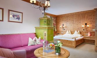 A cozy room with a pink couch, a round table, and a bed with white bedding. The walls are made of wood and there are decorative elements as well as a pendant lamp.
