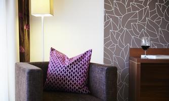 A cozy armchair with a colorful cushion stands next to a lamp. In the background, you can see a decorative wall with leaf patterns.
