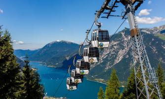 A cable car that travels over a clear lake and green mountains. In the background, beautiful landscapes and a blue sky can be seen.