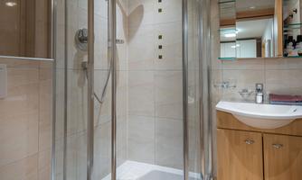 A modern bathroom with a round shower and a sink. The walls are bright tiled and there are wooden cabinets for storage.