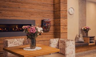 A cozy interior with wooden paneling and a modern fireplace. A vase of flowers is on the table, making the room feel inviting.
