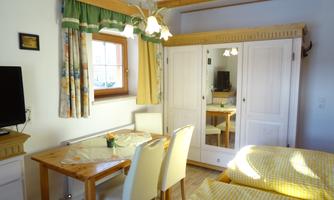 A cozy room with two beds, a table and chairs. There is a television and plenty of natural light from a window.