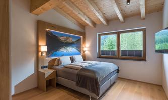 A cozy bedroom with a wooden ceiling and large windows. The bed is modern and decorated with a beautiful landscape picture.