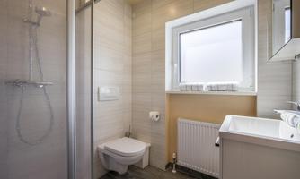 A modern bathroom with a shower, sink, and toilet. The space is bright and well-structured with a window that lets in daylight.