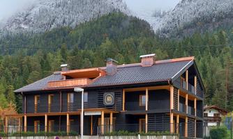 A modern building in the mountains with snow-capped peaks in the background. Surrounded by green trees and a well-kept environment.