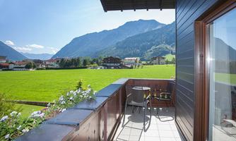 A beautiful view from a balcony overlooking green meadows and mountains. The sun is shining and the sky is blue.