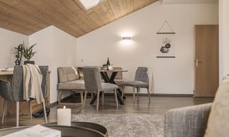 A modern, bright living room with wooden walls and a cozy dining table. The room is stylishly furnished and offers an inviting atmosphere.