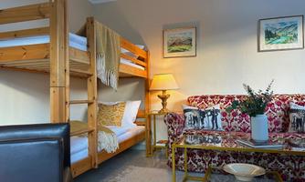 A cozy room with a wooden bunk bed and a red sofa. There is a coffee table with a vase and pictures on the wall.