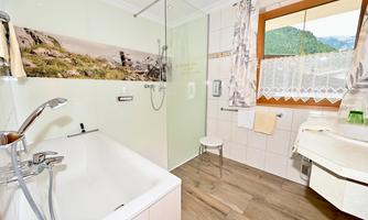 A modern bathroom with a bathtub and a shower. Plenty of daylight through the window and a harmonious color scheme.