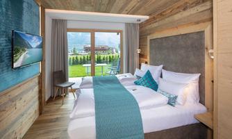 A modern hotel room with two beds and a television. Large windows offer a view of the green landscape.