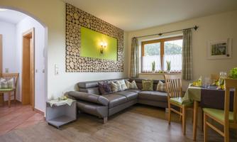A modern living room with a cozy couch and a dining table. The walls are designed in light colors and decorated with wooden ornaments.