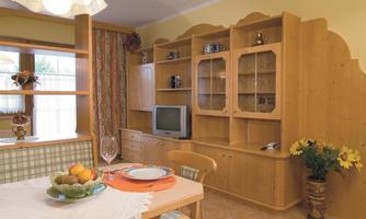 A cozy living kitchen with wooden furniture and a dining table. In the background, there is a television, and on the table, fruits and dishes are decorated.
