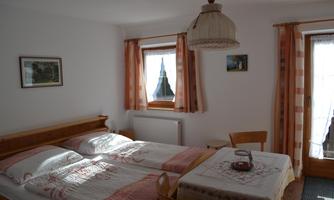 A cozy bedroom with two beds and a table. Large windows let in plenty of light and offer a view outside.
