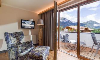 A cozy room with a blooming armchair and a television. The balcony offers a stunning view of the mountains and the surroundings.
