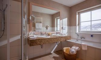 A modern bathroom with a double sink and large mirror. The window offers a view of a beautiful landscape.