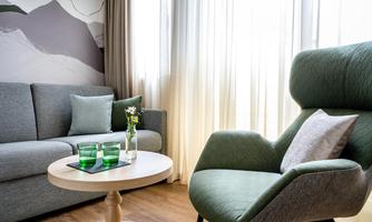 A stylish living room with a gray sofa and a comfortable green armchair. On the table, there is a vase with a flower and drinks.