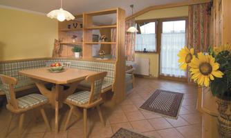 An inviting dining area with a wooden table and a cozy bench. Large windows bring plenty of light into the room, and fresh sunflowers beautify the corner.