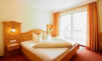 A cozy hotel room with a large double bed and bright curtains. The room has access to a balcony with plenty of natural light.