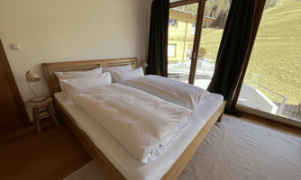 A cozy bedroom with a large bed and plenty of natural light. Large windows offer a view of the green landscape outside.