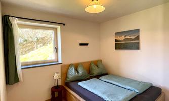 A cozy bedroom with a double bed and two pillows. A window lets in natural light and there is a small nightstand.