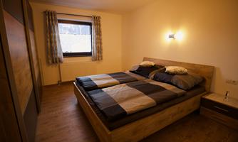 A cozy bedroom with a double bed and wooden floor. The walls are light, and a window provides natural light.
