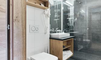 A modern bathroom with a glass shower and elegant dark gray tiles. The fixtures include a sink with wooden shelves and a toilet.