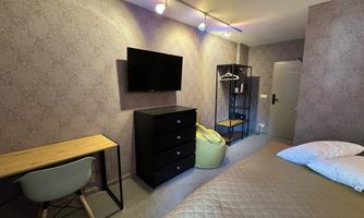 A modern room with a large bed, a desk, and a television. The walls are in a soft gray tone, and there is a cozy seating area.
