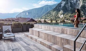 A modern pool on a terrace with a view of the mountains. A woman is standing in the water and enjoying the view.