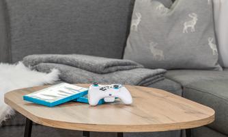 A stylish living area with a modern coffee table. On it lies a game controller and a game case, next to it a cozy blanket and a cushion.