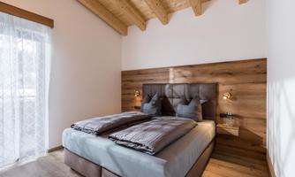 A modern bedroom with a double bed and wood paneling. Large windows let in plenty of light and create a bright, cozy atmosphere.