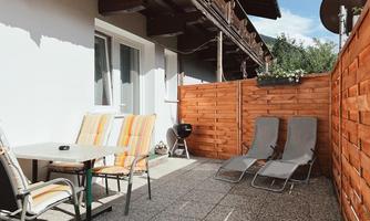 A cozy terrace with garden furniture and sun loungers. The walls are made of wood, and there is a barbecue in the corner.