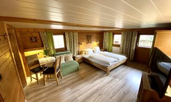 A cozy bedroom with wooden decor and large windows. There is a double bed, a seating area, and a table.