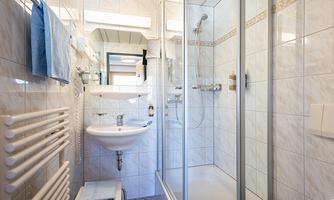 A modern bathroom with a shower, a sink, and towels. The walls are decorated with light tiles.