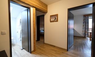 A modern hallway with two open doors leading to a bathroom and a bedroom. A small picture hangs on the wall, and there is a table with chairs in the background.