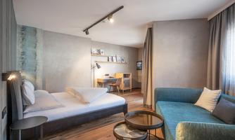 A modern hotel room with a double bed and a cozy seating area. The room is bright and tastefully furnished.