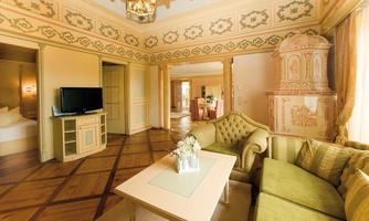 An elegant living room with a green sofa and a table. The walls are tastefully decorated, and a traditional stove is located in the corner.