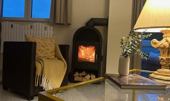 A cozy living space with an armchair, a wood stove, and a table. A warm glow emanates from the lamp and the fire in the stove.