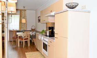 A modern kitchen with light cabinets and a wooden dining table. The room is well-lit and invitingly designed.