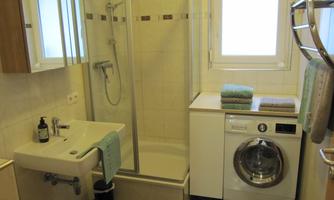 A modern bathroom with a shower, a sink, and a washing machine. Towels and toiletries are neatly arranged.