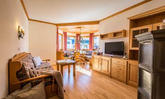 A cozy living room with wooden furniture and a large window. There is a couch, a table, and a television.