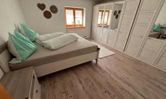 A modern bedroom with a large bed and soft pillows. The room features a mirror wardrobe and has light wooden floors.