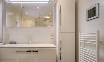 A modern bathroom with white walls and a large mirror. There is a stylish sink unit and a heated towel rail.